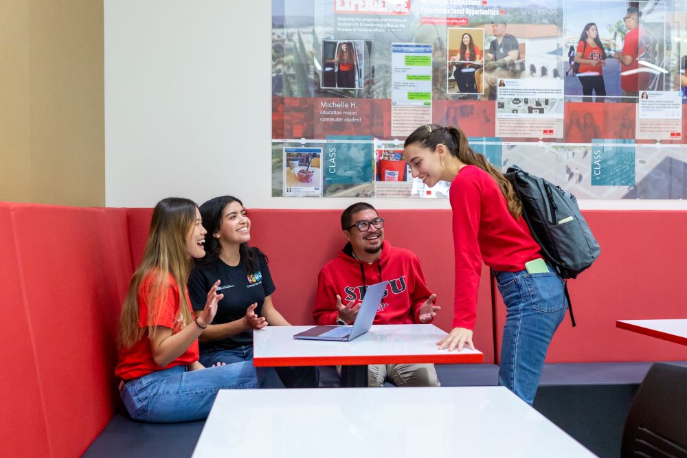 student standing at table and talking to three students